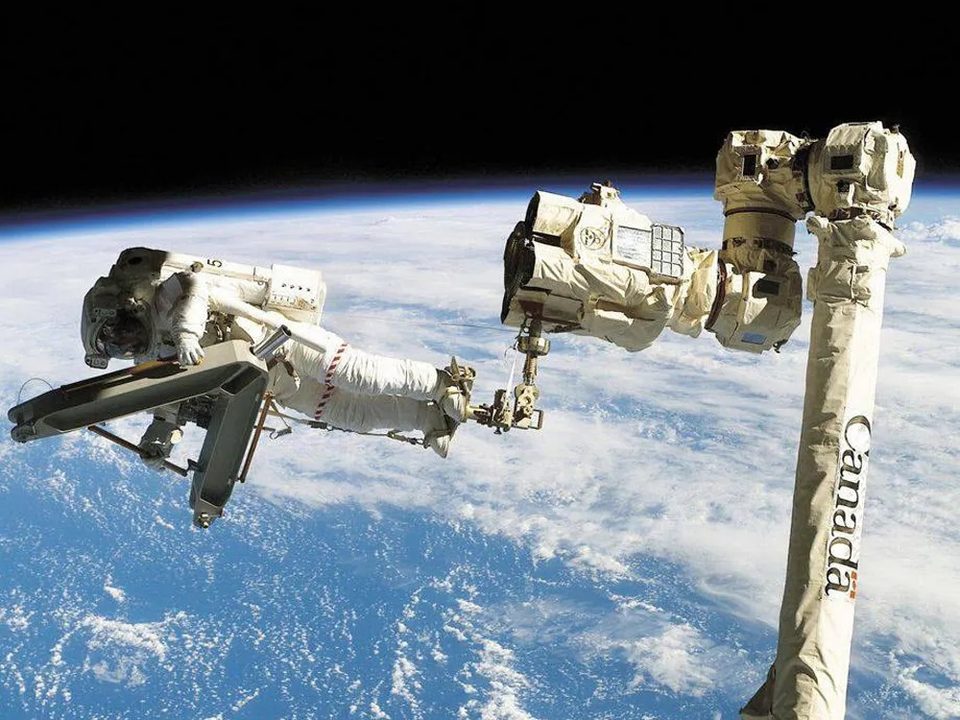 Astronaut Stephen Robinson riding Canadarm2 over Earth during STS-114